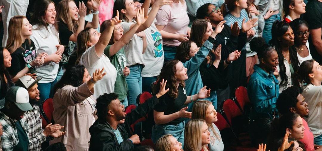 Crowd of college students raising their hands, singing to God