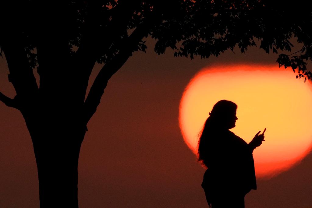 A woman looks at her phone while watching the sun set in Kansas City, Mo.