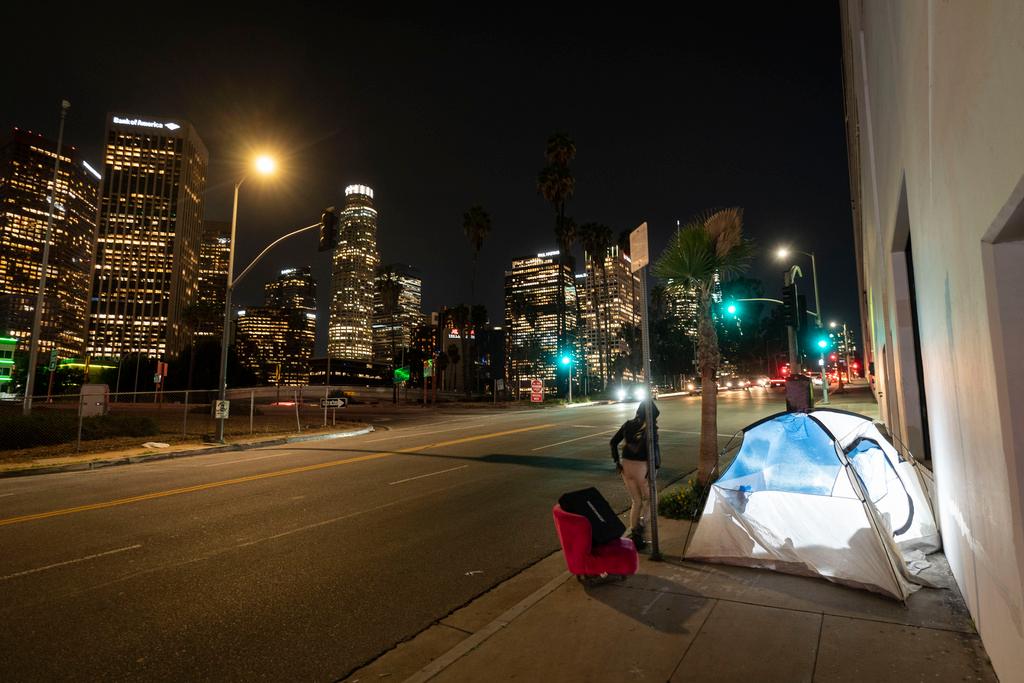 Woman walks past a homeless person's tent with a chair in downtown Los Angeles