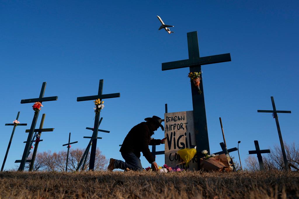 A plane takes off from Ronald Reagan Washington National Airport as Roberto Marquez of Dallas places flowers at a memorial of crosses he erected for the 67 victims of a midair collision between an Army helicopter and an American Airlines jet