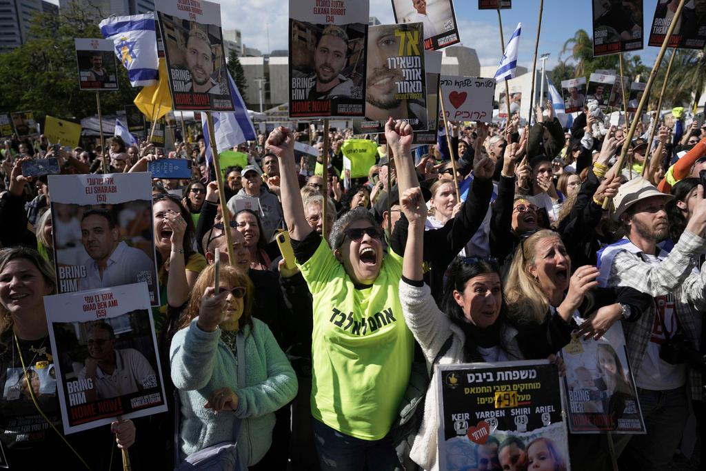 People holding posters with photos of Israelis hostages Eli Sharabi, Or Levy and Ohad Ben Ami, react at the so-called "hostages square" as they watch their release live on a television screen in Tel Aviv