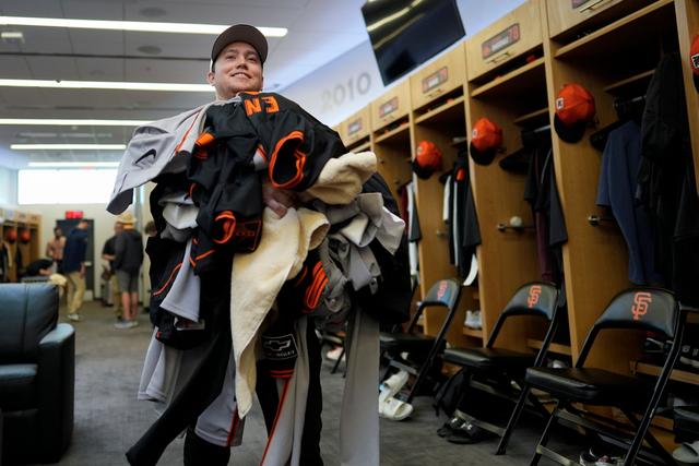 San Francisco Giants clubhouse attendant Riley Halpin gathers a mound of dirty clothes in the clubhouse after spring training baseball practice at the team's facility in Scottsdale, Ariz.