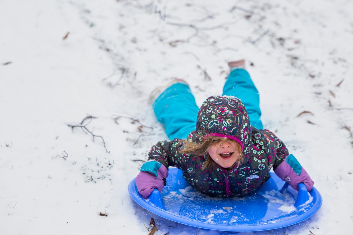 Little girl on a sled, smiling and wearing brightly colored snow clothes