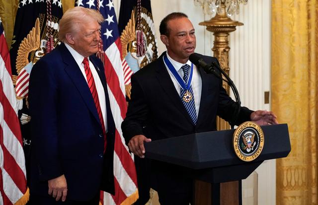 President Trump standing next to Tiger Woods at a podium with American flags behind them.