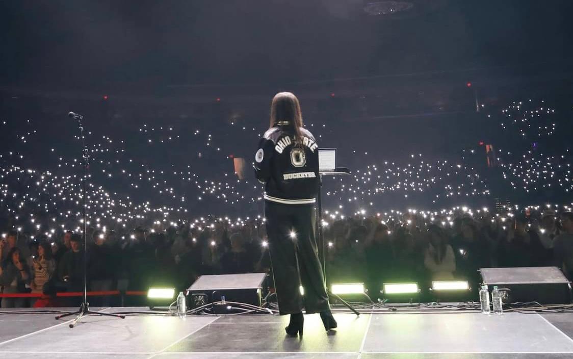 The back of a woman in front of a huge crowd with their lights brightly shining from their cell phones