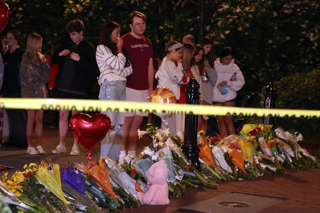 An impromptu memorial shared online brings students bearing flowers into the evening near the center of the Florida State campus in sight of the Student Union building