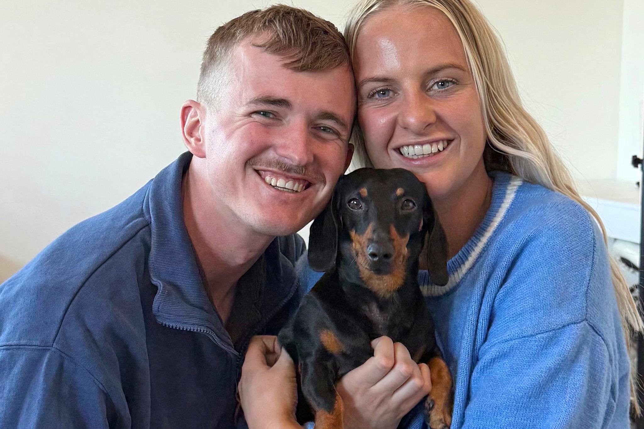 Smiling couple holding their small dog in between them.