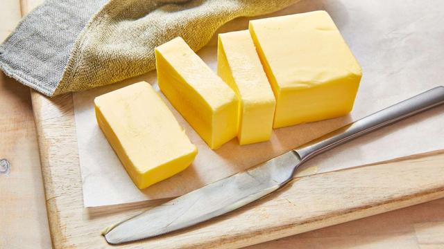 Sliced butter on a cutting board with a butter knife sitting next to butter