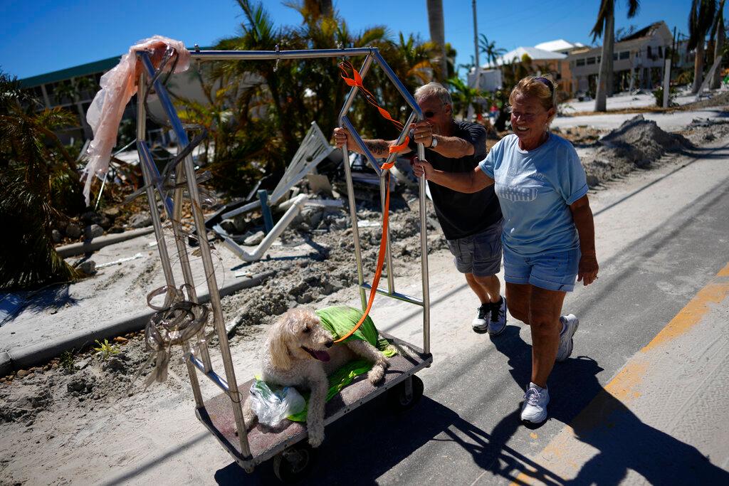 Debbie and Lou Evans push their dog Brody on a hotel luggage cart they found amidst the wreckage, as they come to check on their home, two days after the passage of Hurricane Ian, in Fort Myers Beach, Fla.