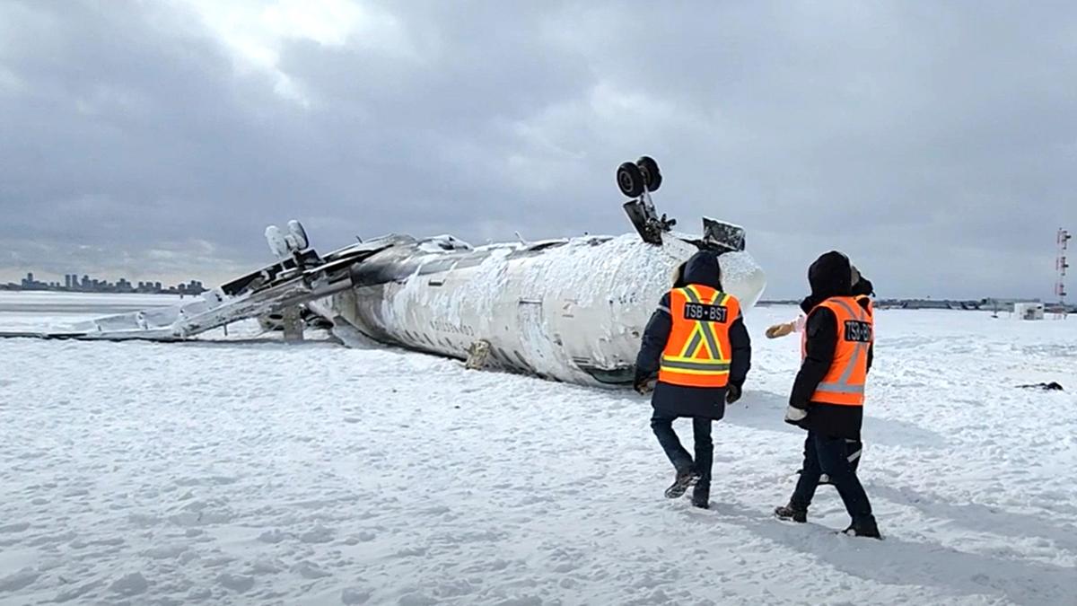 Aviation personnel in the snow with the crashed Delta aircraft