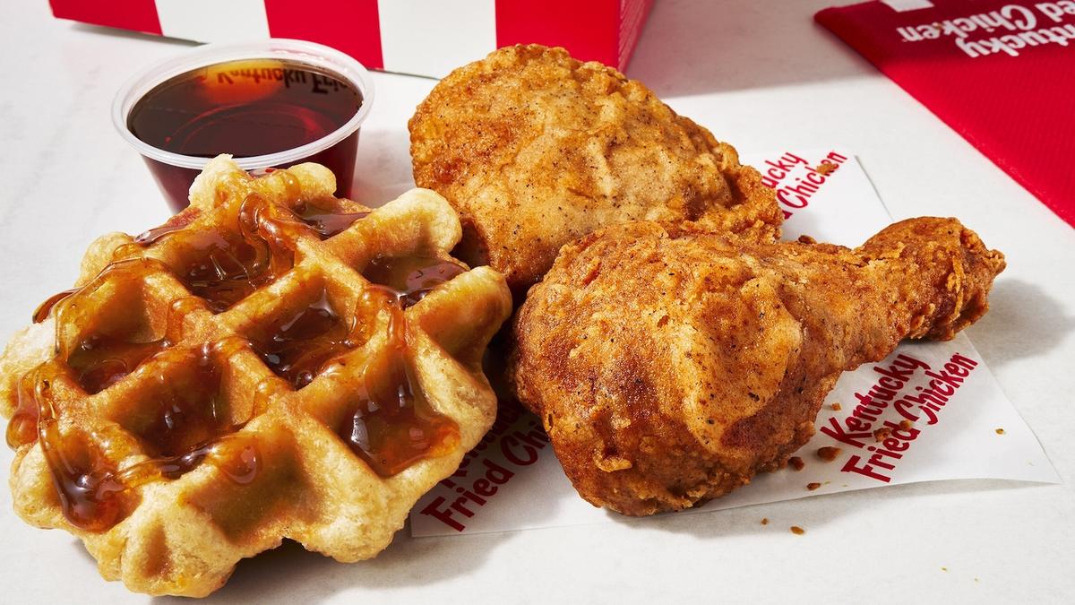 A small waffle pictured next to two pieces of breaded, fried chicken and a cup of syrup