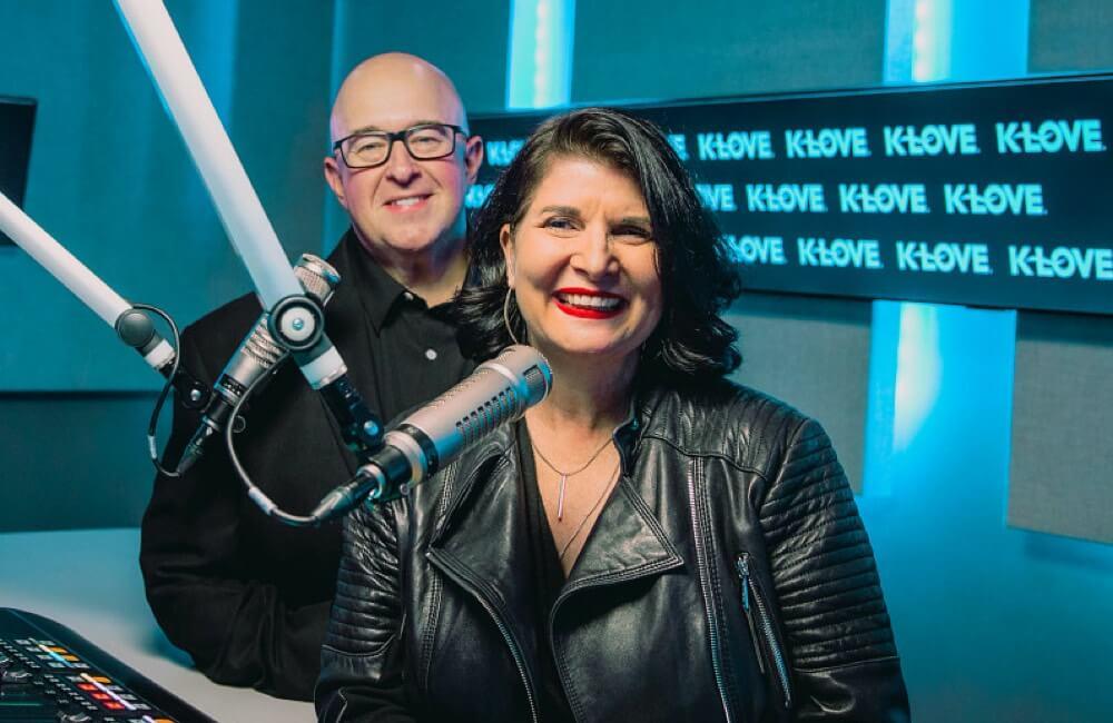 Scott and Kelli smiling together in the k love studio with microphones