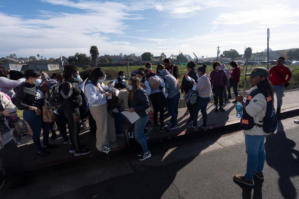 Migrants stand in groups as they arrive at a bus stop after leaving a processing facility in San Diego